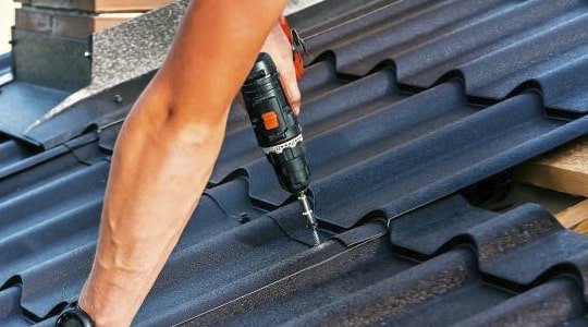 Hombre instalando una lámina de acero sobre el techo de una casa