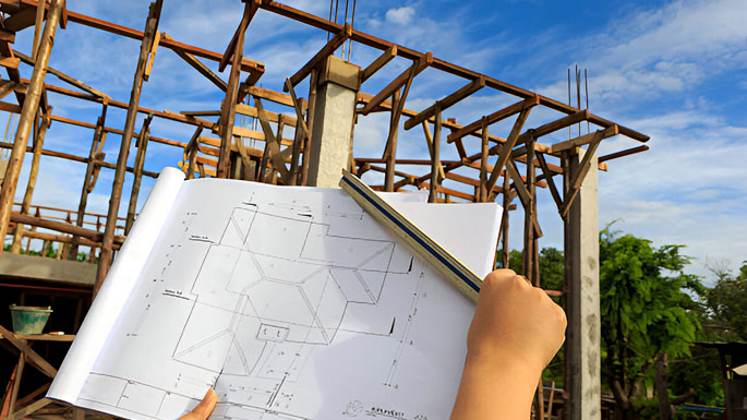 Manos sosteniendo un plano arquitectónico delante de una obra en construcción
