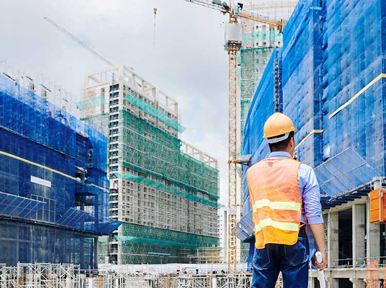 Ingeniero con casco de seguridad parado frente a diversos edificios en construcción